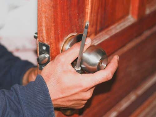 Emergency locksmith holding screwdriver and testing doorknob